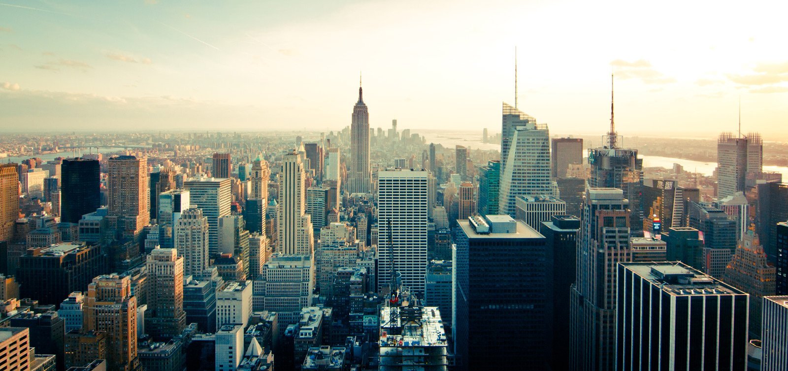 Cityscape of New York City with the Empire State Building prominent, seen at sunset.