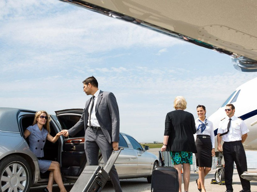Woman exiting a limousine; man assists with luggage, near a private jet; airport setting.